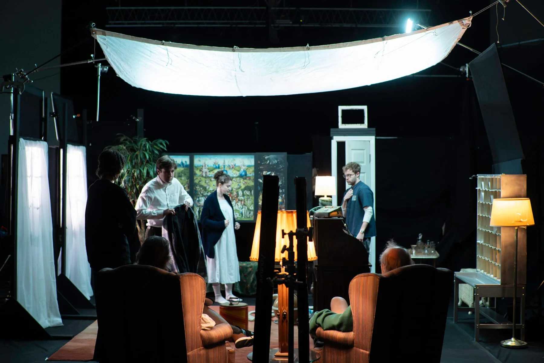 Cast and crew work beneath a large soft light on the film set.