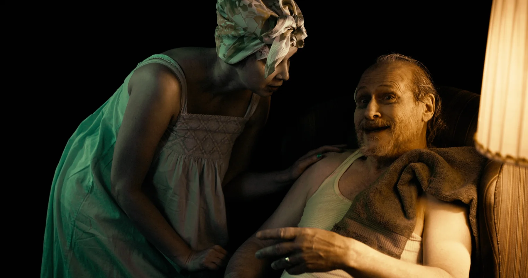 Two characters speak in a warmly lit room surrounded by darkness.